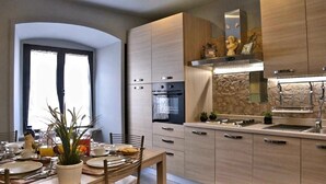A modern kitchen with built-in appliances, a dining area with a table set for two, and a stone backsplash. - Beautiful Colosseum Roma (Rome)