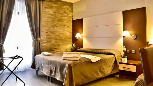 A modern hotel room with a bed, bedside tables, a wall-mounted lamp, and a window with curtains. - Beautiful Colosseum Roma (Rome)