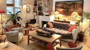 A cozy living room with a sofa, armchairs, a coffee table, a bookshelf, and a fireplace. - Loft Dans le Quartier Latin (Paris)