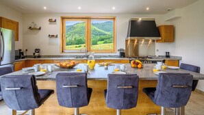 A modern kitchen with a large island, bar stools, and a view of green hills.