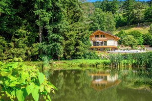 Ein Holzhaus mit Balkon, umgeben von dichtem Wald und einem Teich.