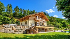 A two-story wooden house with a balcony, stone wall, and a swimming pool.