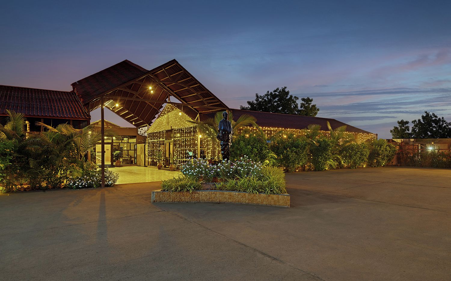 Un hotel con un área exterior cubierta, una estatua y jardines bien iluminados.