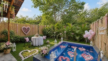 Un patio trasero con piscina, un arreglo floral con forma de corazón y una valla de bambú.