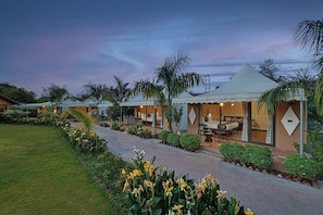 A series of connected bungalow-style accommodations with outdoor seating areas, surrounded by well-maintained gardens and palm trees. - Soil to Soul Resort - Statue of Unity (Tilakwada)