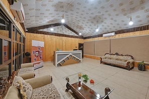 A reception area with a wooden reception desk, a sofa, a glass coffee table, and a bulletin board with information. - Soil to Soul Resort - Statue of Unity (Tilakwada)