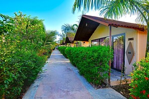 A pathway flanked by lush greenery and a row of buildings with a distinct architectural style.