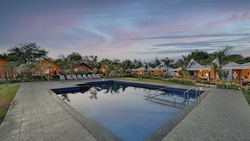 Un resort con piscina, sillones de descanso y bungalós sobre el agua.