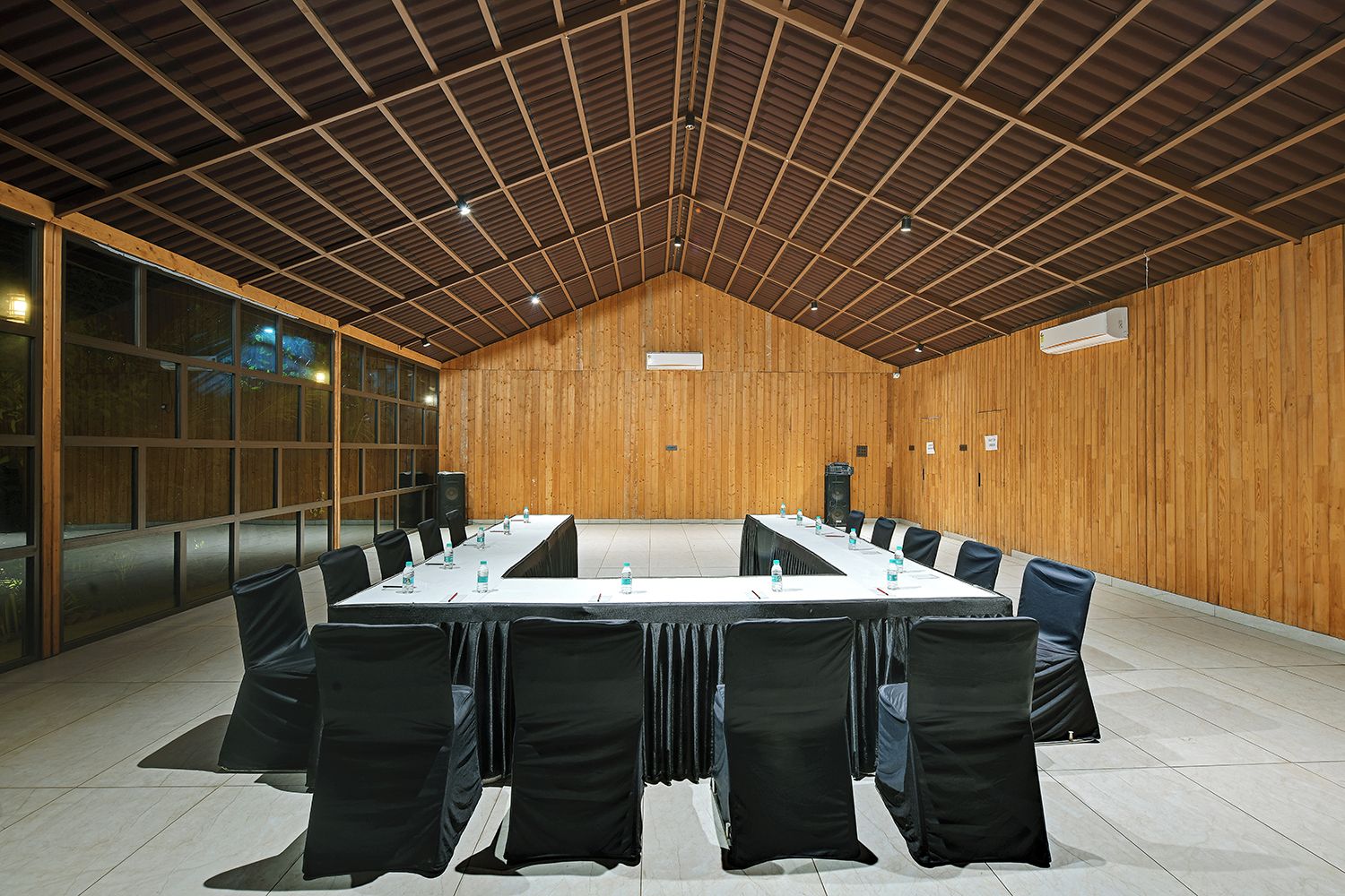 Un salón de conferencias con una larga mesa, sillas negras y decoración de madera.