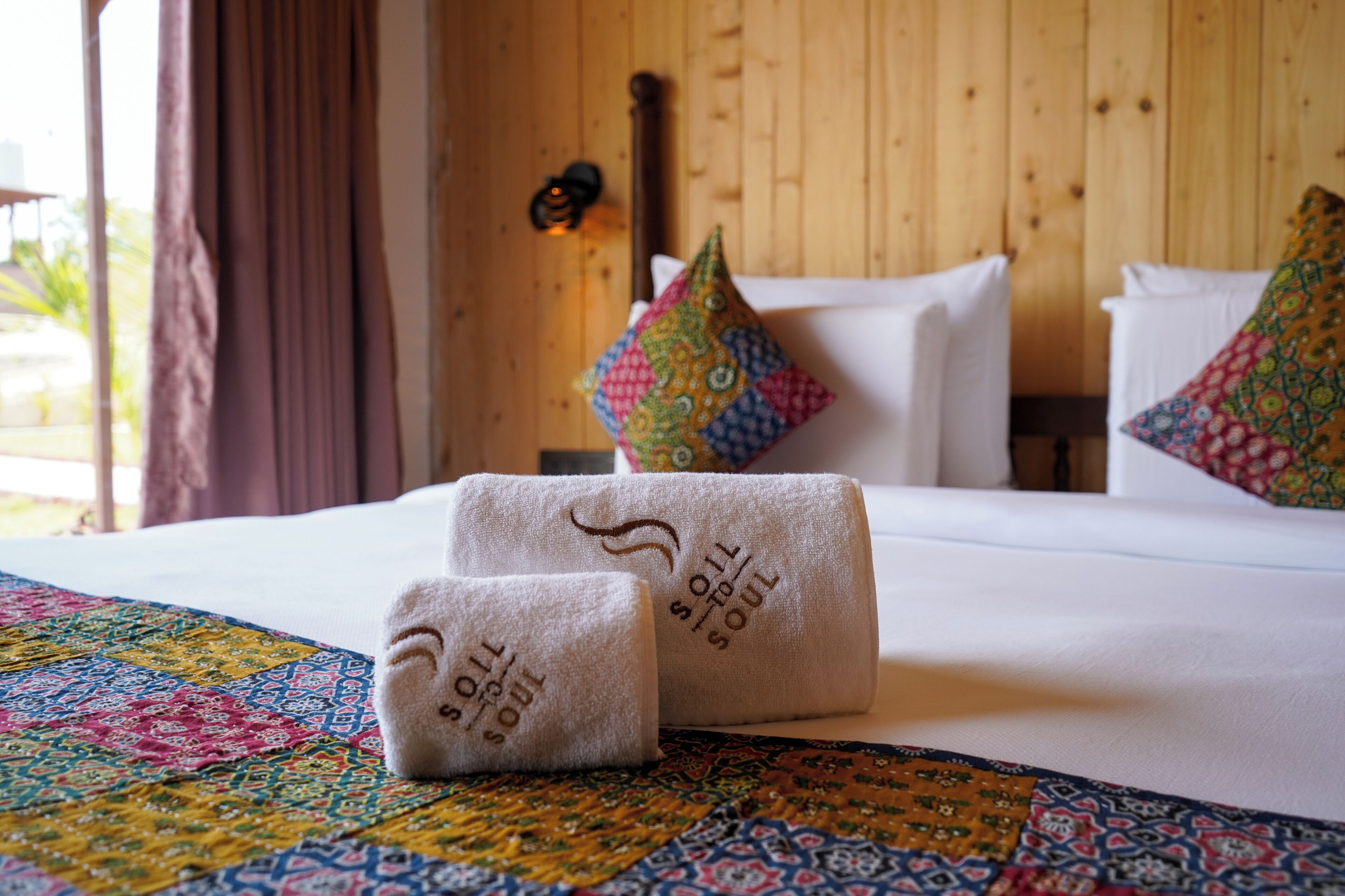 A neatly made bed with white linens and a colorful quilt, pillows with patterned designs, and a wooden headboard.
