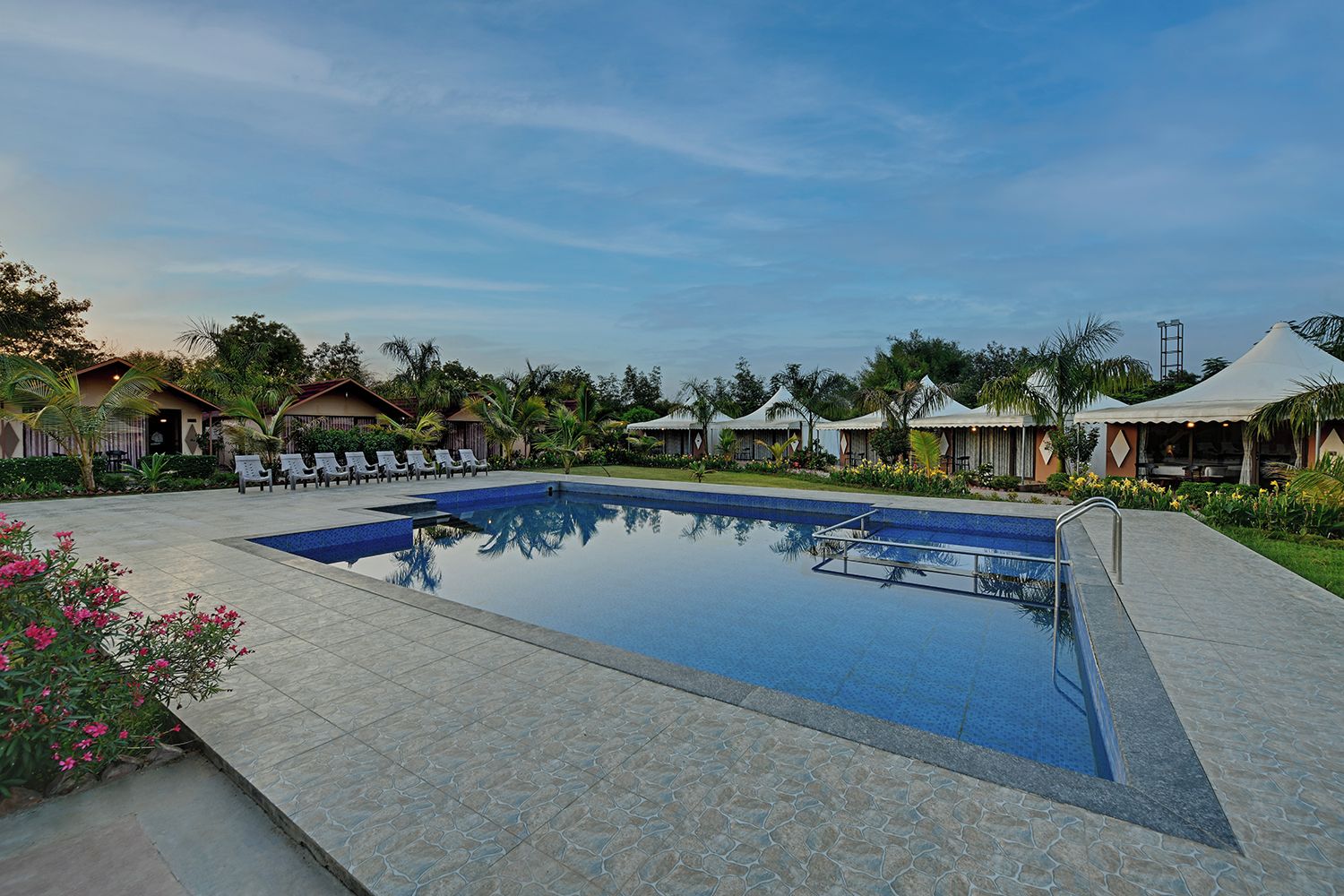 Una piscina con sillas de descanso y sombrillas, rodeada de edificios con estilo de resort.