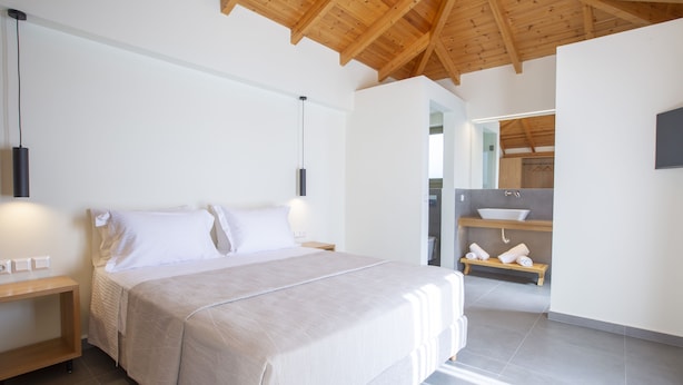 Un dormitorio con una cama grande, mesitas de noche, techo de madera y un baño con lavabo y toallero.