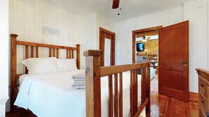 Un dormitori amb un llit de fusta, una paret blanca amb un rètol i una porta de fusta que dona a una altra habitació.