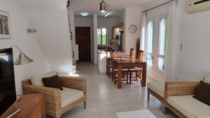 A modern living room with wicker furniture, a dining area with wooden chairs, and a kitchen in the background. - Cyprus, 2 Beds Ensuite, Pool, Patio, Wifi, Parking (Polis)
