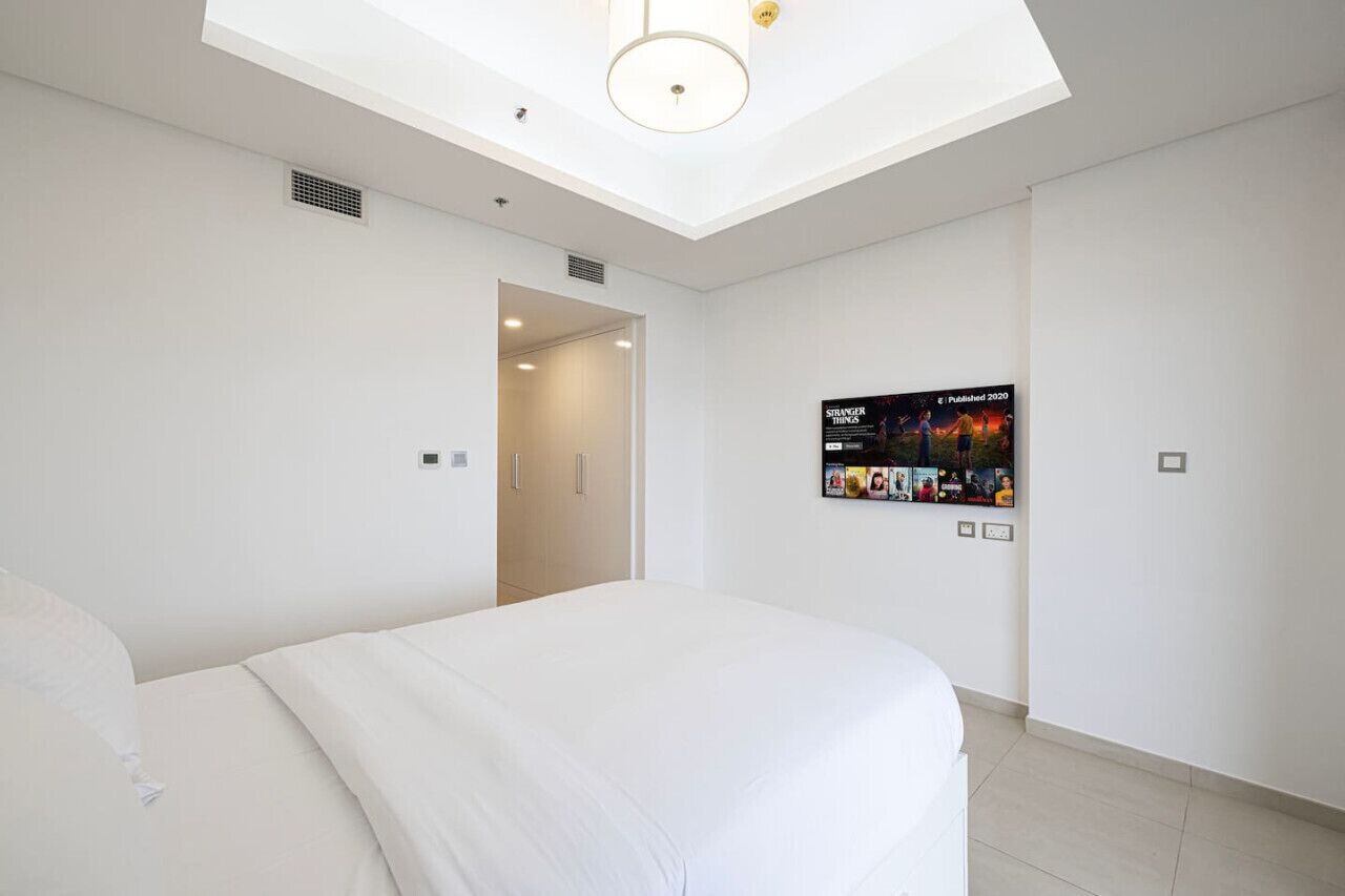 A modern hotel room with a skylight, a large bed, and a wall-mounted TV displaying a movie poster.