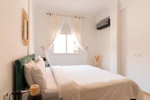 A neatly arranged bedroom with a bed, a bedside table, a lamp, and a window with curtains.