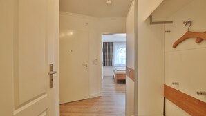 A hotel room with a wooden floor, a bed, a wooden hanger, and a white wardrobe.