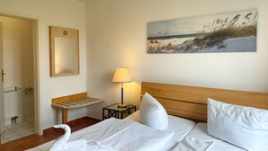 Une chambre d’hôtel avec un lit, un banc, une lampe et un tableau représentant une scène de plage.