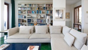 Un salón con un sofá blanco grande, una estantería llena de libros y un cuadro en la pared.