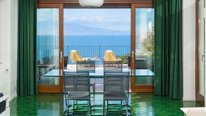 Un balcón con una mesa y sillas de vidrio, vista al mar y suelo con baldosas verdes.