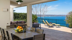 Un área de comedor al aire libre con una mesa preparada para cuatro, un sofá y vista al mar.
