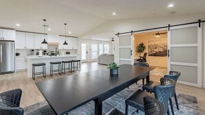 A spacious kitchen with a central island, modern pendant lighting, and a sliding glass door leading to a dining area with a large table and chairs. - Papago Haven, Private Oasis in Old Town (Scottsdale)