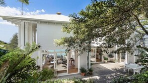 Een modern huis met een overdekt terras, grote ramen en een tuin met diverse planten.
