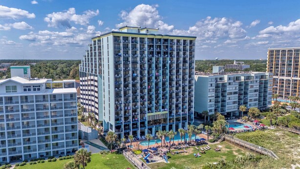 Um hotel moderno com várias varandas, piscina e área ajardinada bem cuidada.