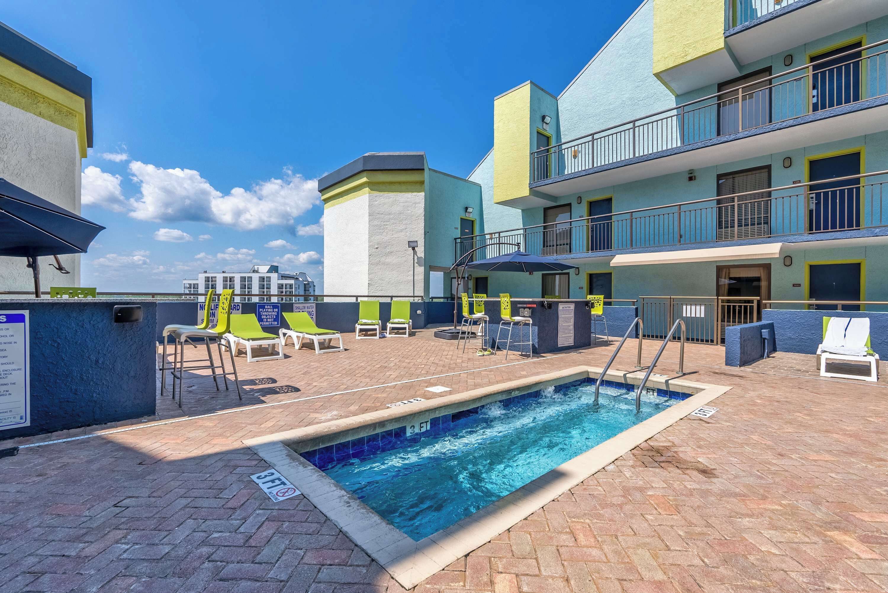 A rooftop pool area with a swimming pool, lounge chairs, and a multi-story building in the background.