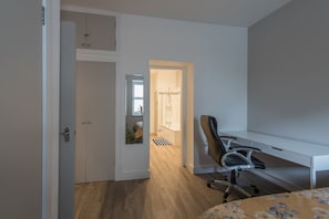 A bedroom with a bed, a desk, and a chair. There is a door leading to a bathroom with a shower and a mirror. - Haymarket - City Centre (Edinburgh)
