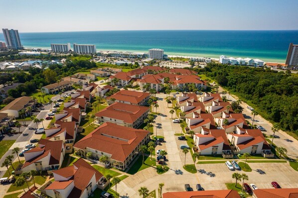 An aerial view of a coastal residential area with multiple buildings, a parking lot, and a beach in the background.