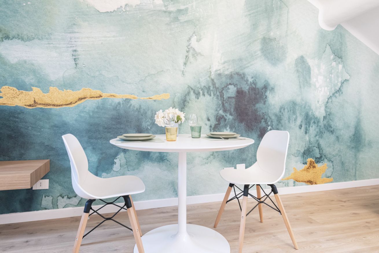Comedor moderno con una mesa redonda blanca, dos sillas blancas y una pared con textura y arte abstracto.