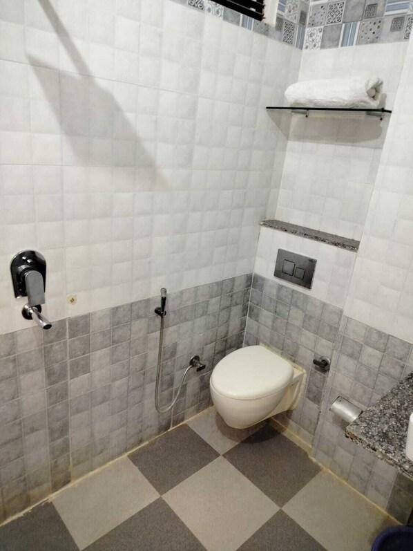 Un baño con inodoro blanco, zona de ducha y perchero para toallas.