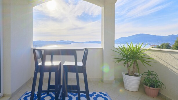 Ein Balkon mit Tisch und Stühlen, zwei Blumentöpfen und Blick auf ferne Berge.