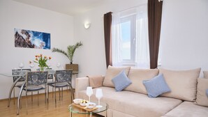 Ein modernes Wohnzimmer mit einem beigefarbenen Sofa, einem Glastisch und einem Essbereich mit Tisch und Stühlen.