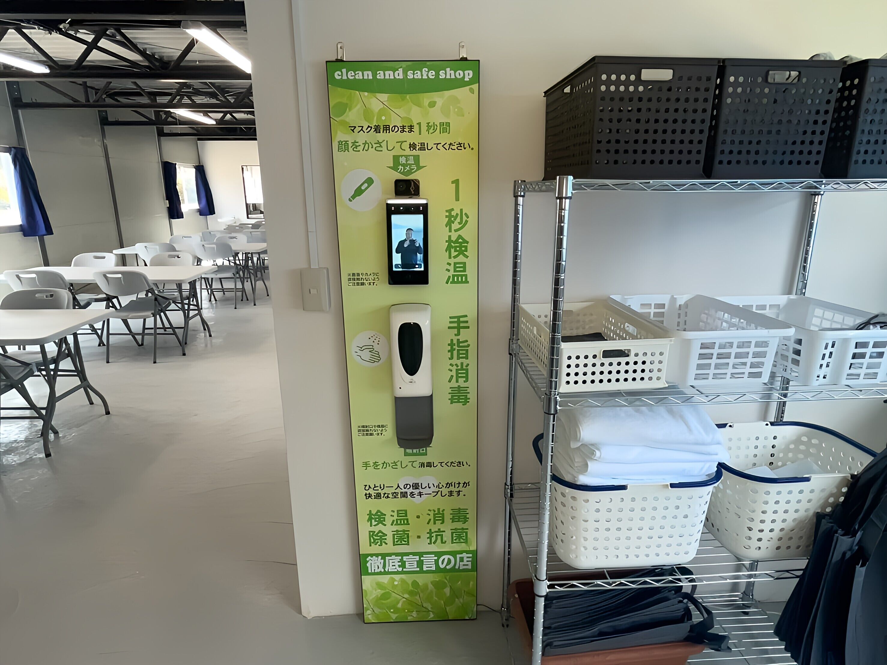 A clean and safe shop with a sanitizer dispenser, a sign in Japanese, and a room with tables and chairs.