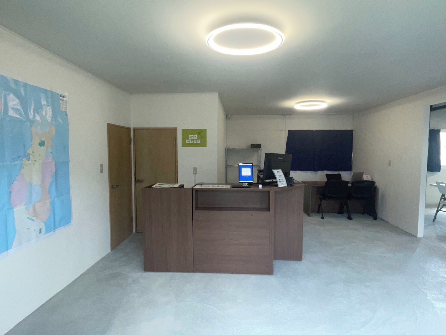 A reception desk with a computer, a chair, a door, and a poster on the wall.
