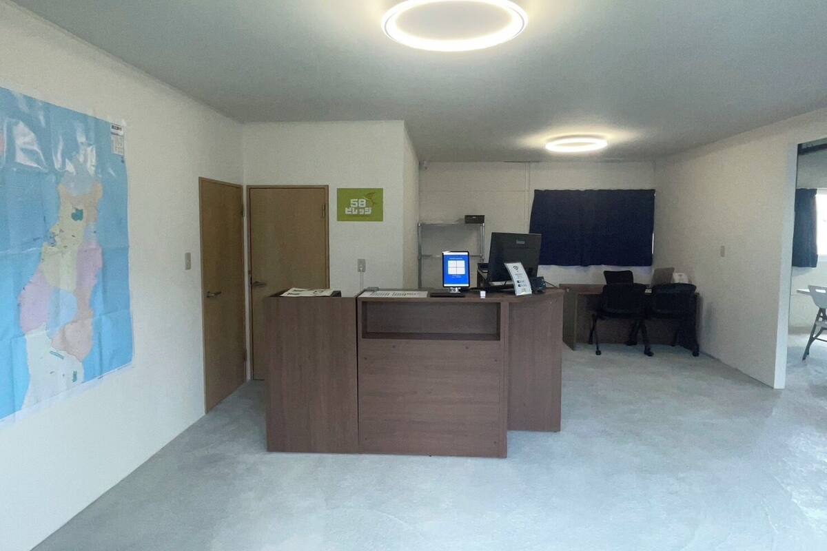 A reception desk with a computer, a chair, a door, and a poster on the wall.