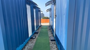 Ein Gang mit blauen Containern, einem grünen Teppich und einem Kiesweg.