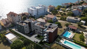 Ein Luftbild eines Wohngebiets mit modernen Gebäuden, einem Schwimmbad und freiem Blick auf das Meer.