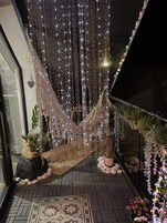 A hammock suspended between two walls, decorated with hanging lights and surrounded by potted plants and decorative stones.