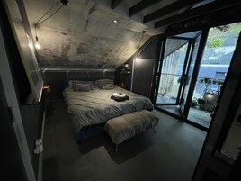 A modern bedroom with a large bed, a bench, and a sliding glass door leading to a balcony.