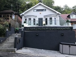 A modern two-story house with a white facade, a balcony, and a dark grey wall in front.