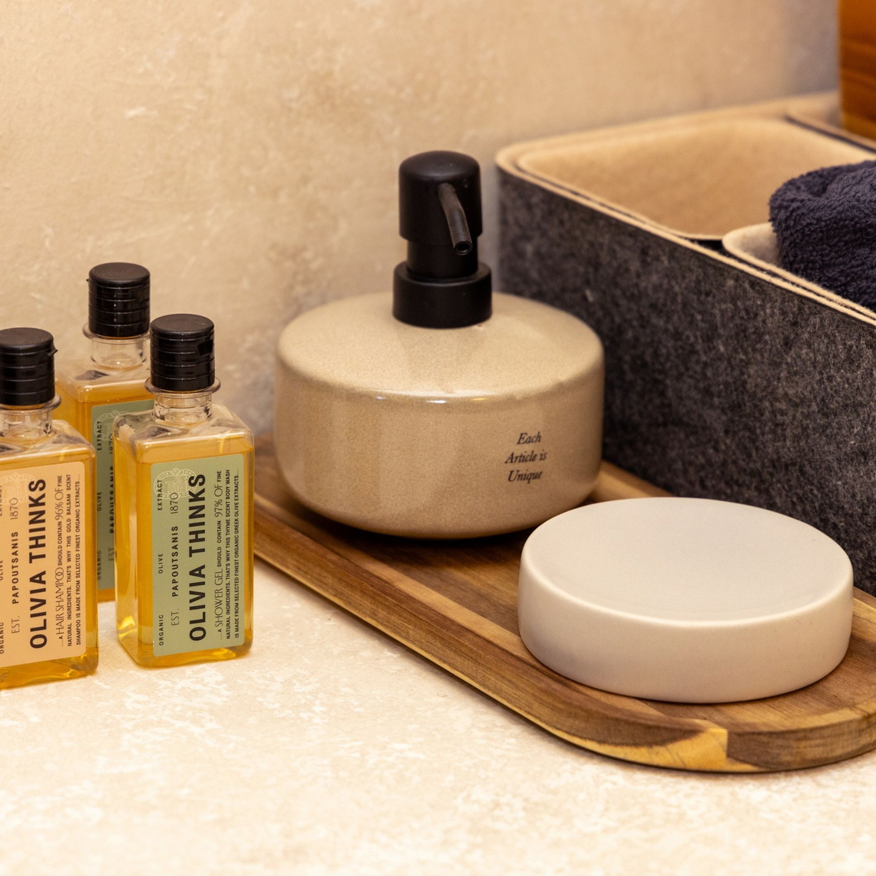 Un vassoio di legno con diversi articoli da toilette, tra cui bottiglie d'olio d'oliva, bagnoschiuma e un portasapone.