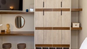 A modern bedroom with a large wardrobe, a flat-screen TV, a mirror, and two stools. - The Hydor Element Of Gaea (Tinos)