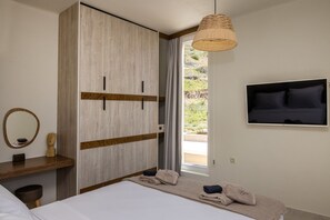 Une chambre à coucher avec un lit, une armoire, un miroir, une télévision et une fenêtre avec des rideaux.