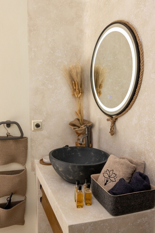 A bathroom with a large round mirror, a black basin, a wicker basket, and a small wooden box.