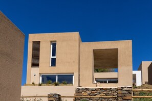 A modern building with a flat roof, large windows, and a stone base. - The Aether Element Of Gaea (Tinos)