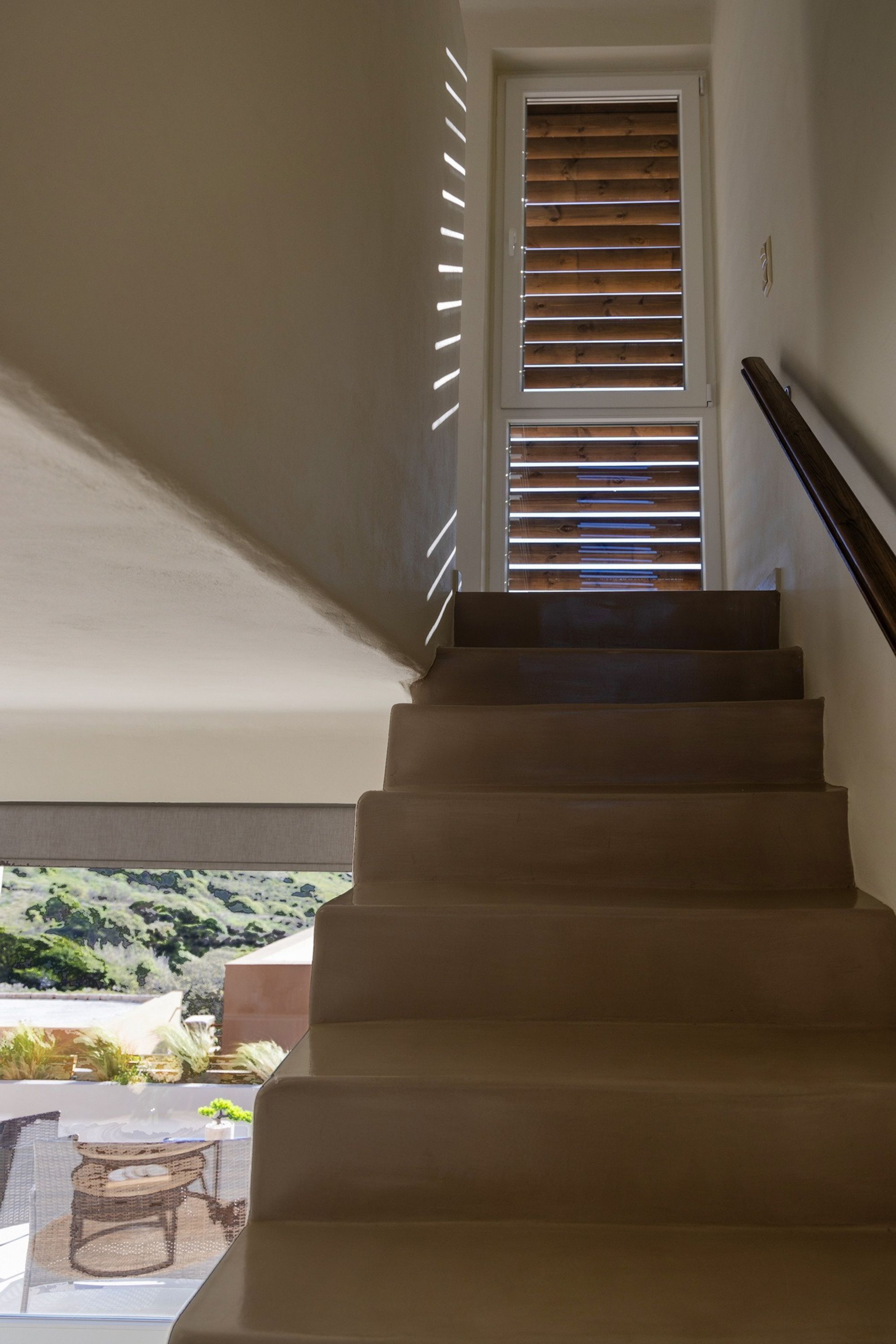 A staircase with wooden steps and a view of a balcony with outdoor furniture.