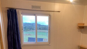 A small bedroom with a single bed, a window with a view of a green field, and a wooden floor. - Mobile Home au Ranch du Bonheur, Évasion à la Ferme (Tourtouse)